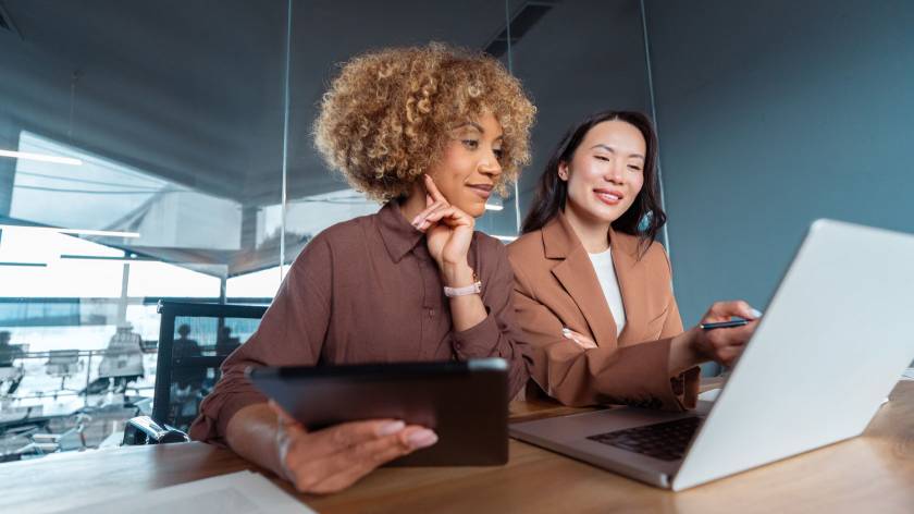 Two professionals collaborate using a laptop and tablet in a modern office, reflecting how businesses can streamline document workflows, reviews and approvals with AI-powered tools.